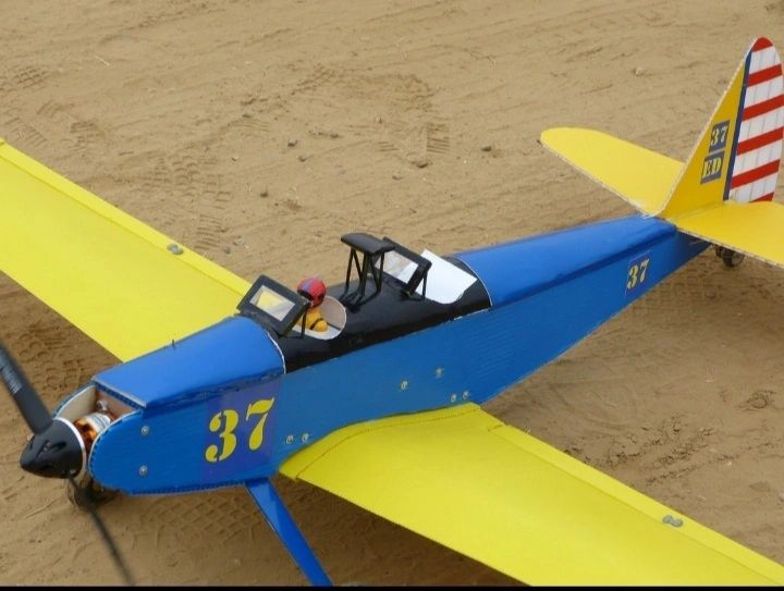 Model airplane with blue body and yellow wings on a sandy surface